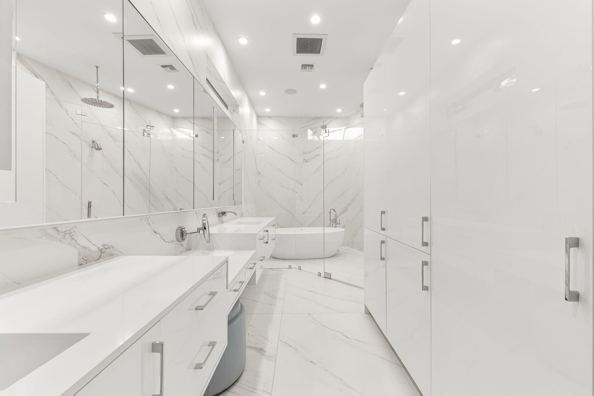 Luxurious white bathroom with marble walls, large vanity, and a soaking tub.