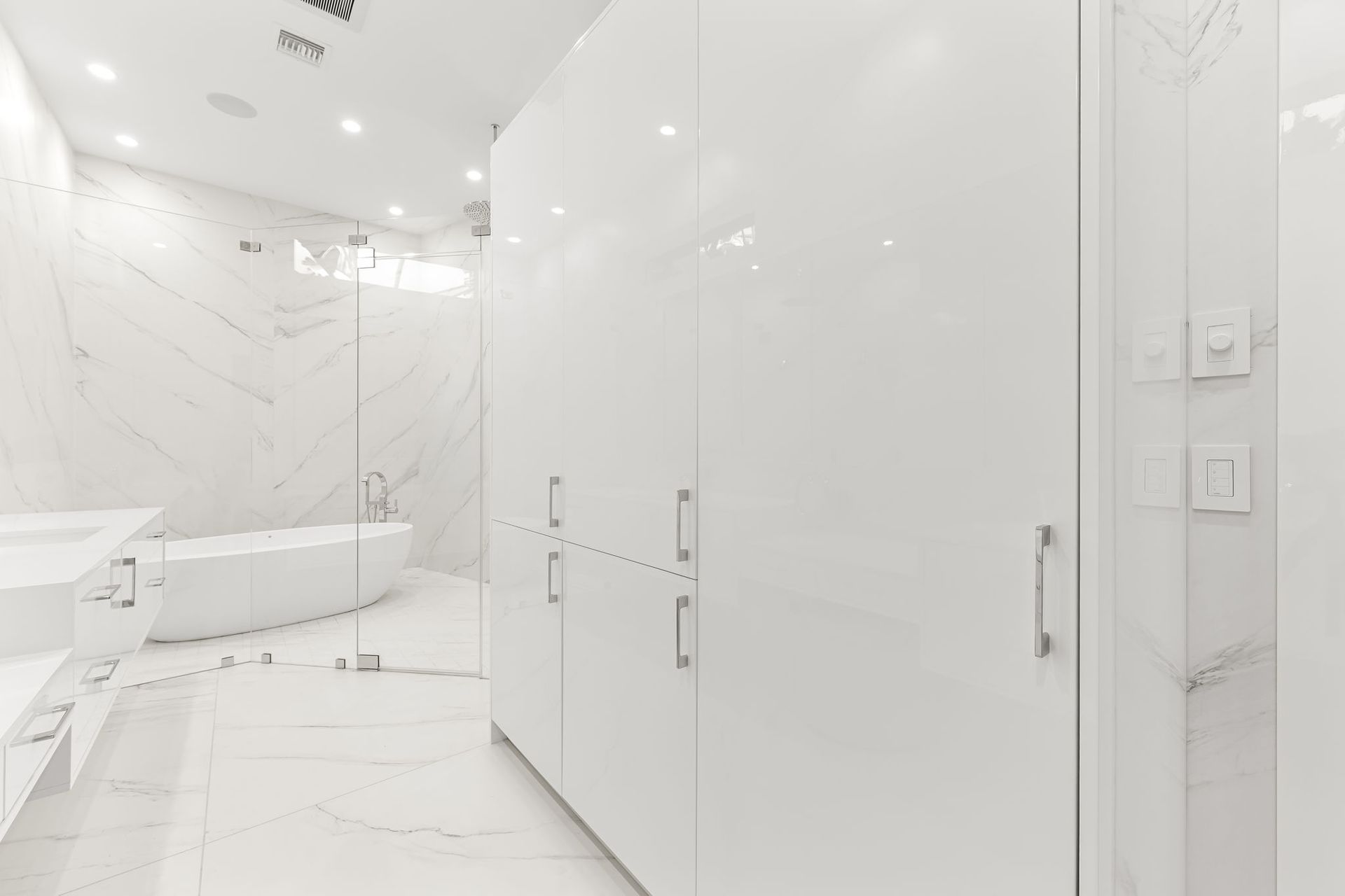 White modern bathroom with marble walls, a large cabinet, and a bathtub.