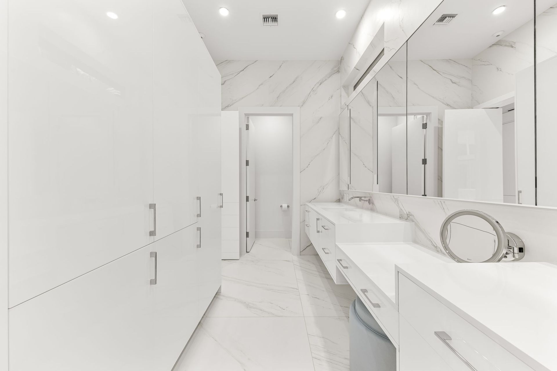 Bright white modern bathroom with marble accents, long vanity, and tall cabinets.