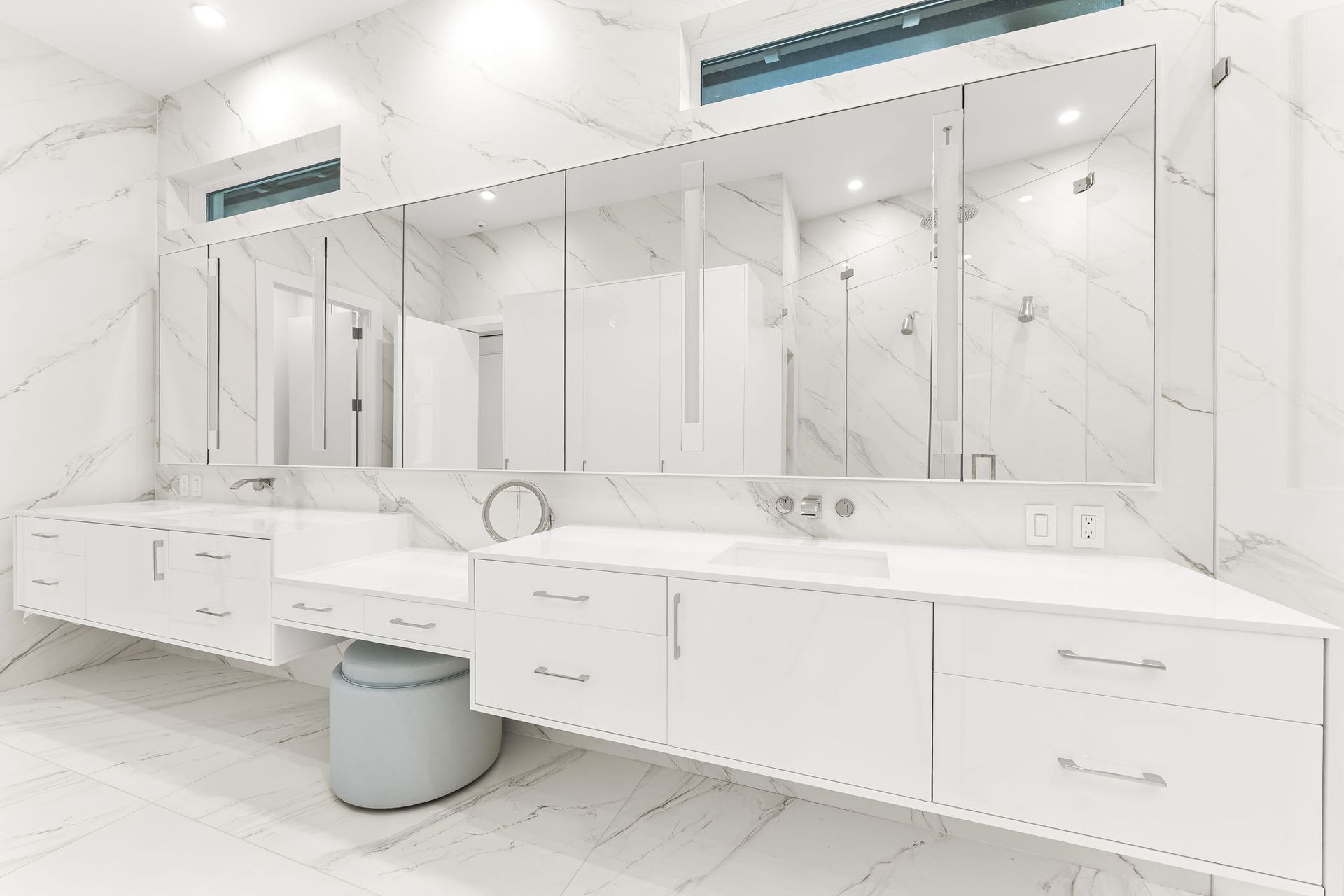 White bathroom with double sinks, marble walls, and large mirrors.