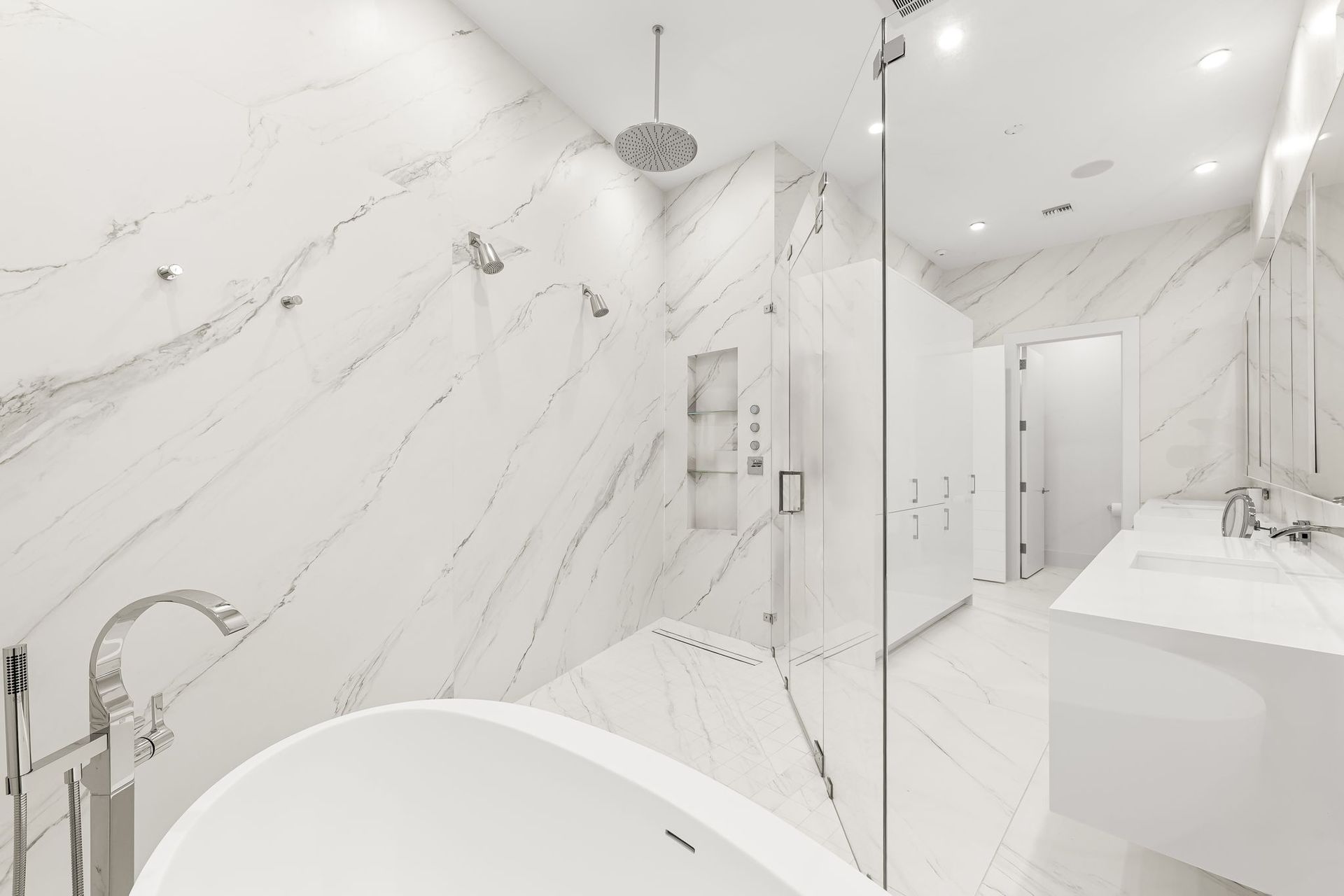 Luxurious all-white bathroom with marble walls and a glass-enclosed shower.