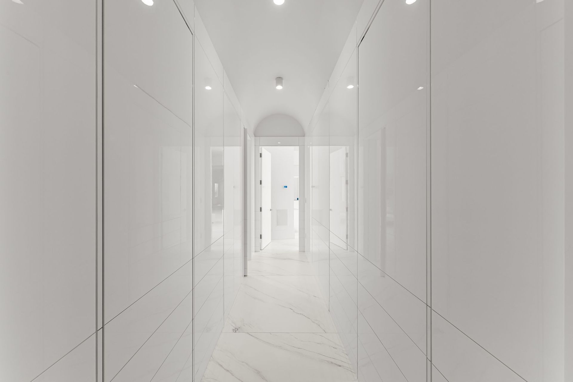 Long, white hallway with glossy closet doors, marble floor, and recessed lighting.