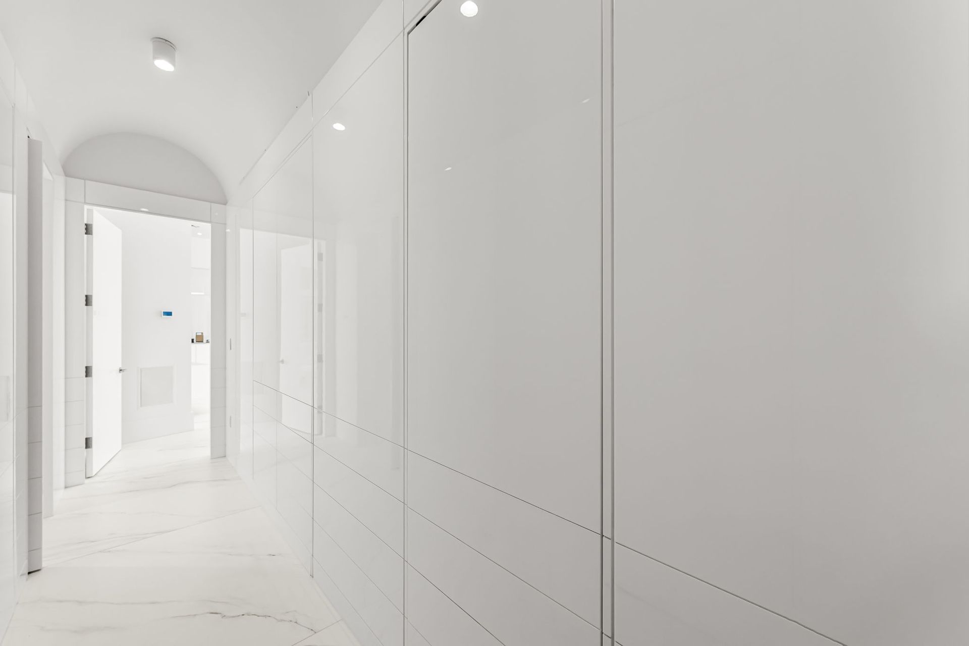 White hallway with glossy walls, recessed lighting, and open doors.