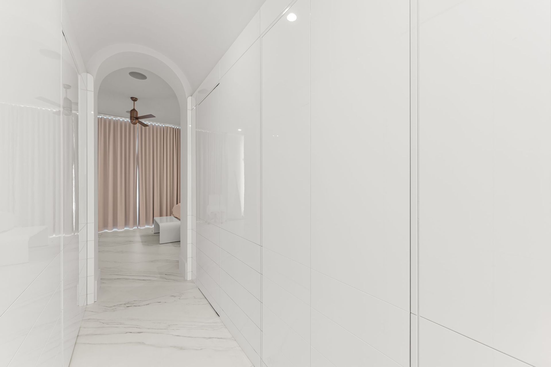 White hallway with tall, closed cabinets on one side and an open doorway to a bedroom at the end.