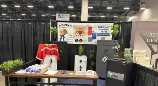 Trade show booth with black drapes, a banner, table displays, and product samples.