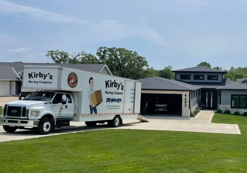 Movers loading cardboard boxes into a white delivery van at a building entrance
