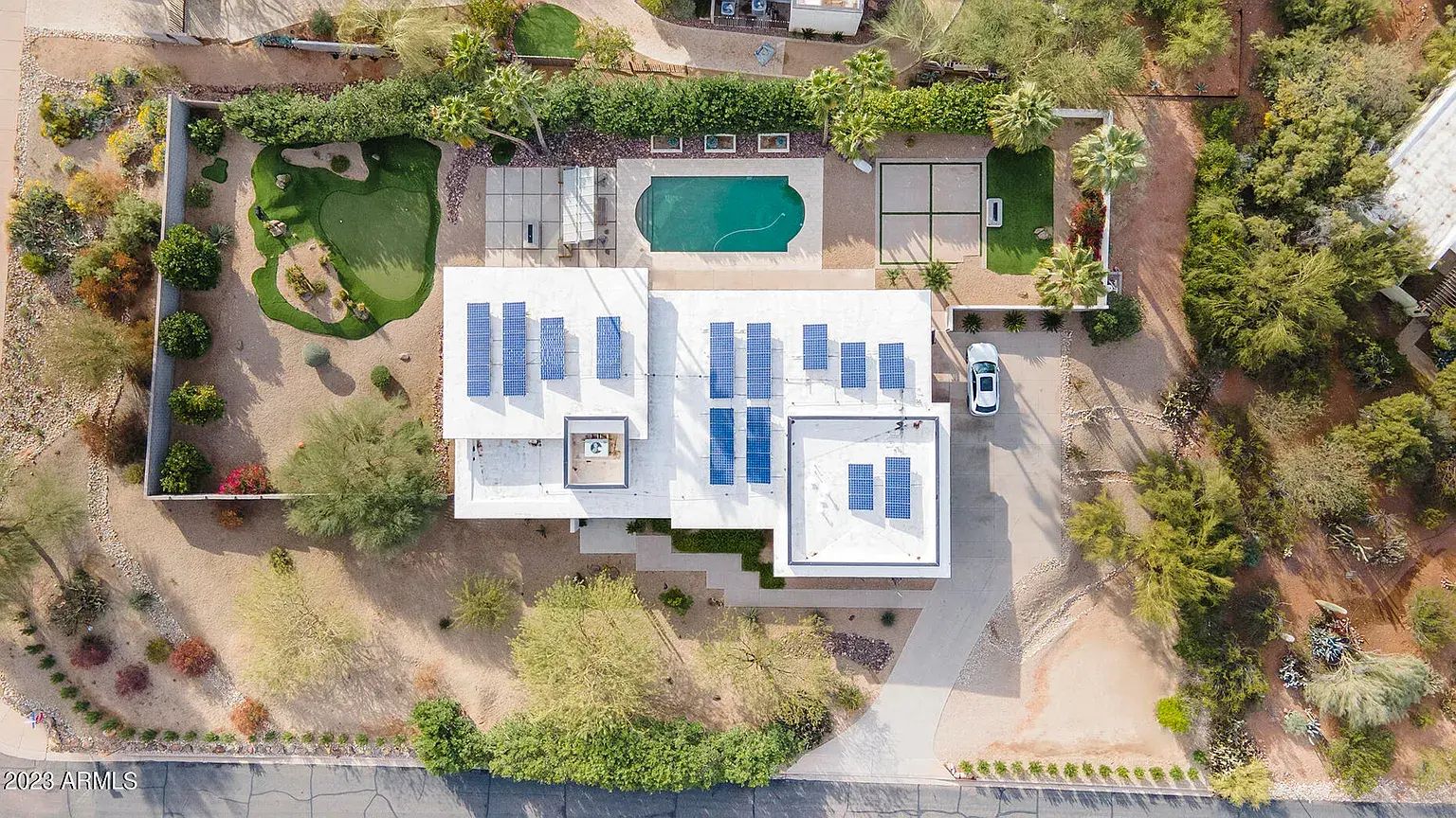 Aerial view of a house with solar panels on the roof and a backyard pool, surrounded by trees and landscaping