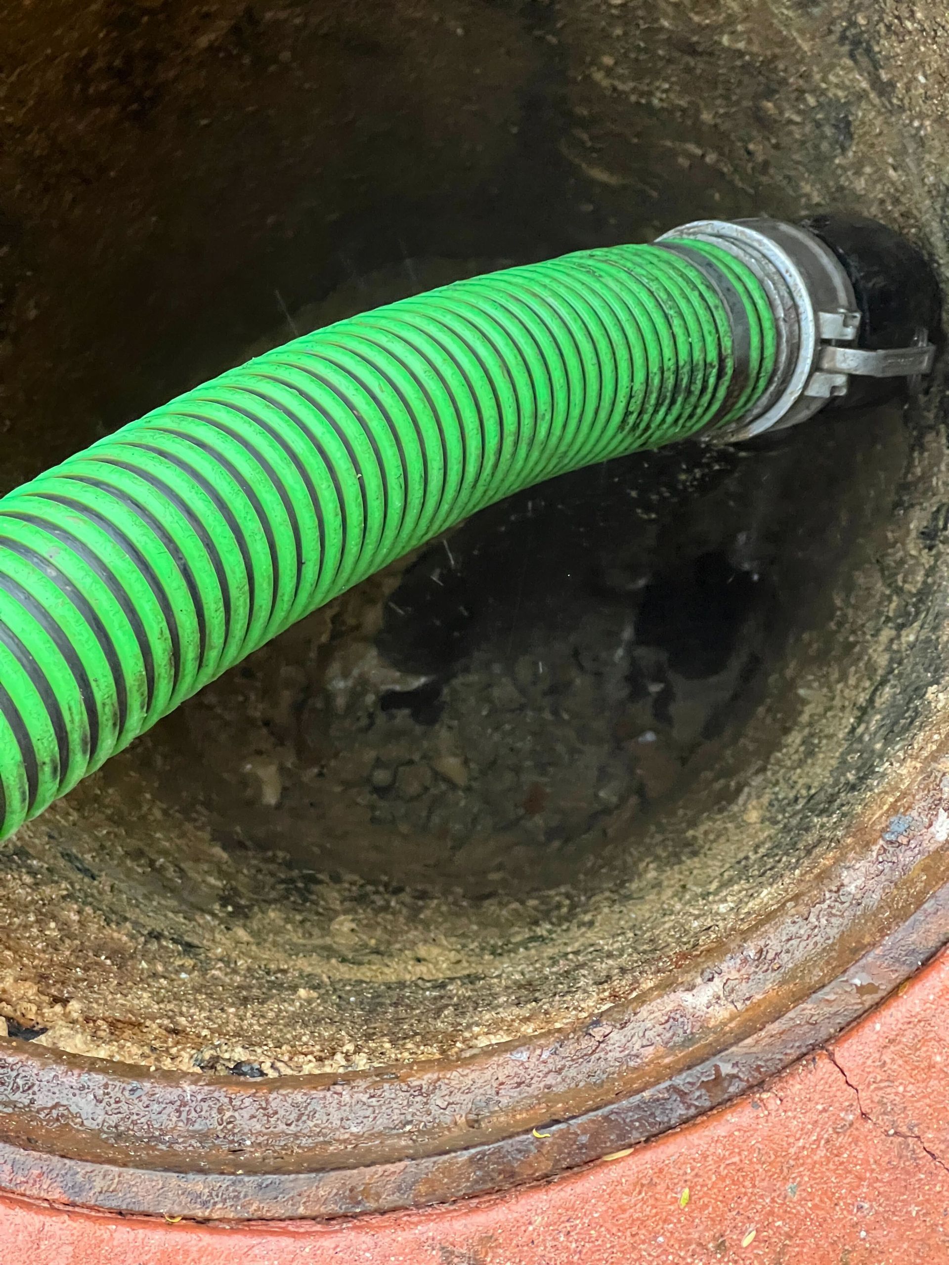 Bright green corrugated hose secured in a rusty drain opening