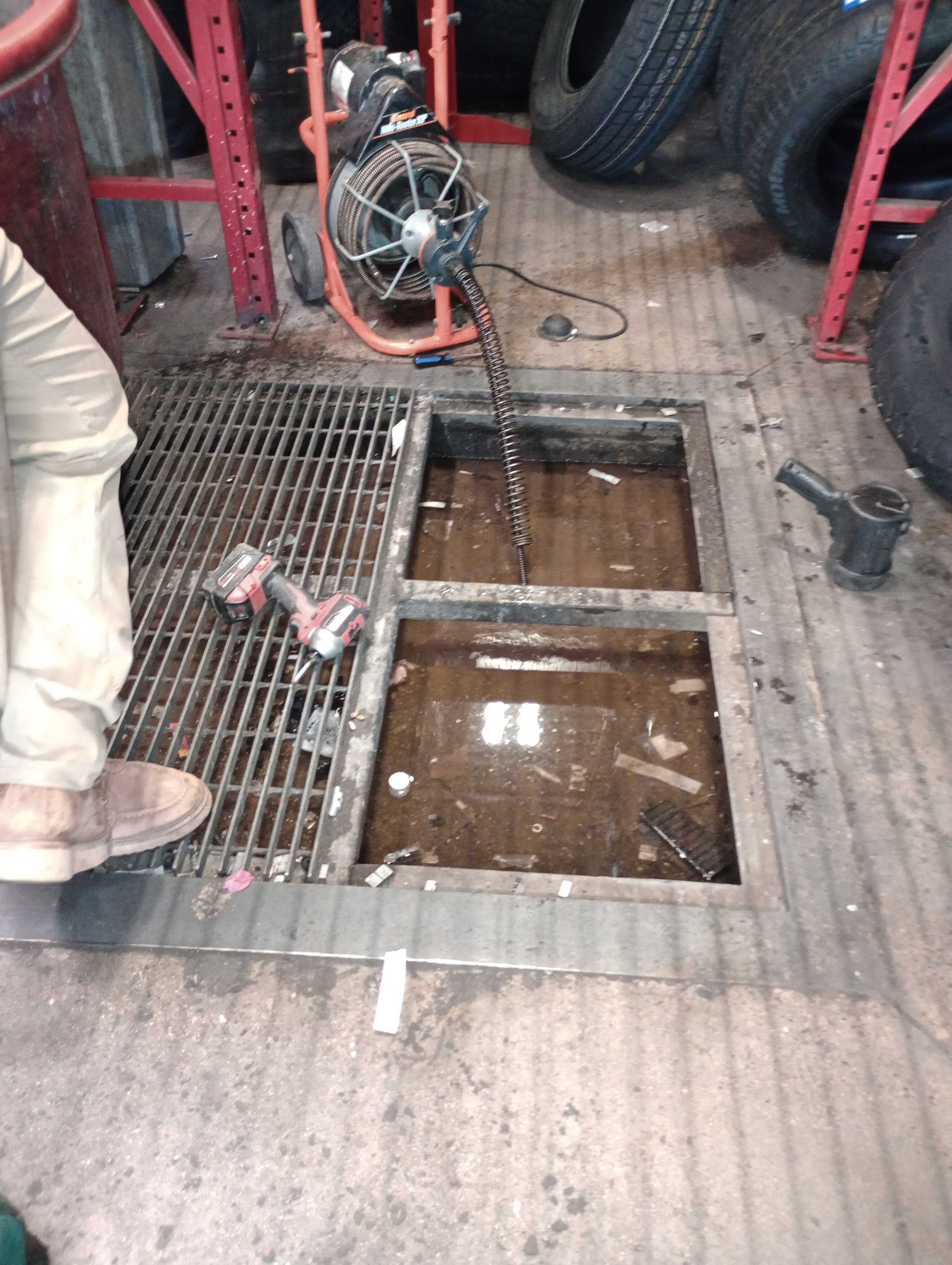 Open floor hatch in a garage with a hose reel and tires nearby