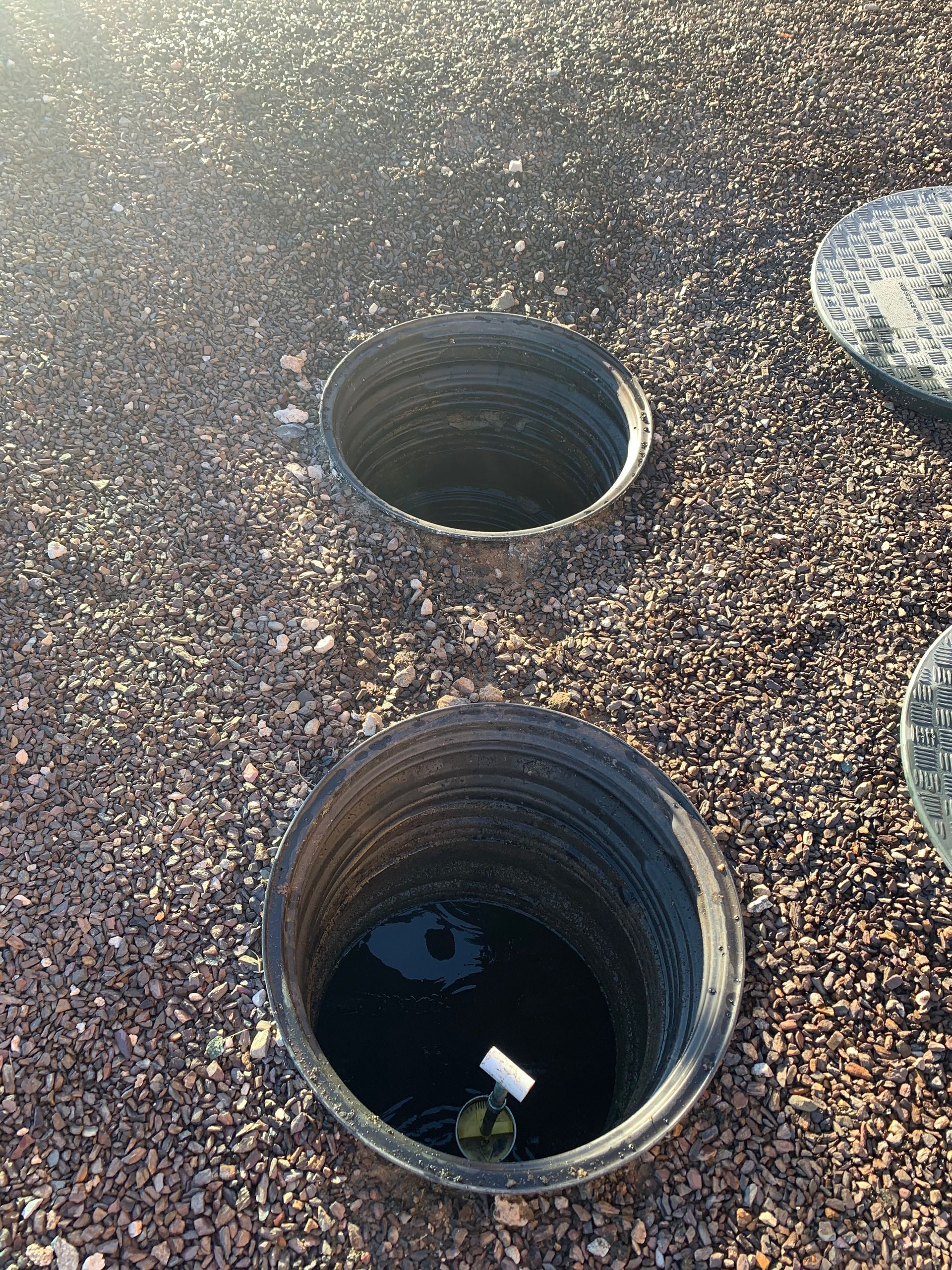 Two open cylindrical ground holes in gravel, one dark pipe opening in the foreground.