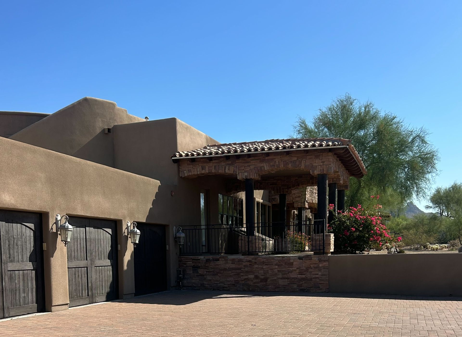 Adobe-style house with stucco walls, dark garage doors, and a covered patio under a blue sky