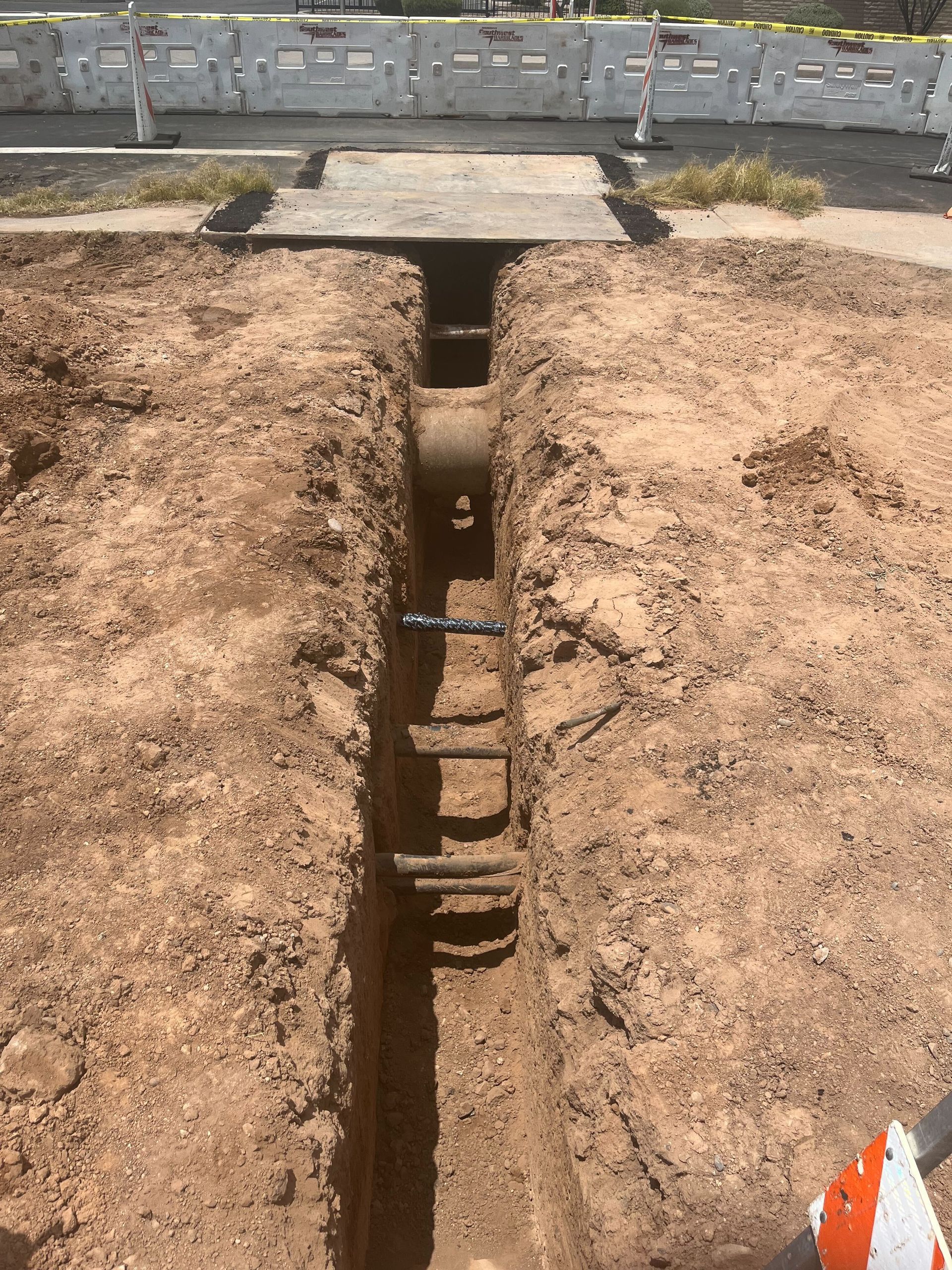 Trench cut through dry soil, with wooden steps and a concrete wall in the background.