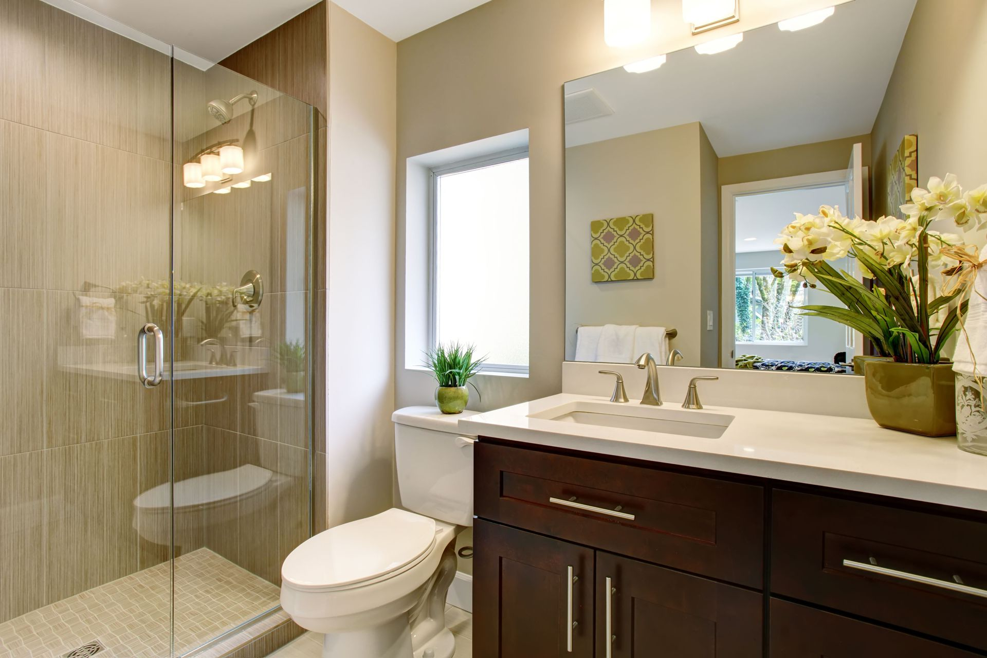 Modern bathroom with shower, toilet, dark cabinets, and flowers. Light tan walls and white countertops.
