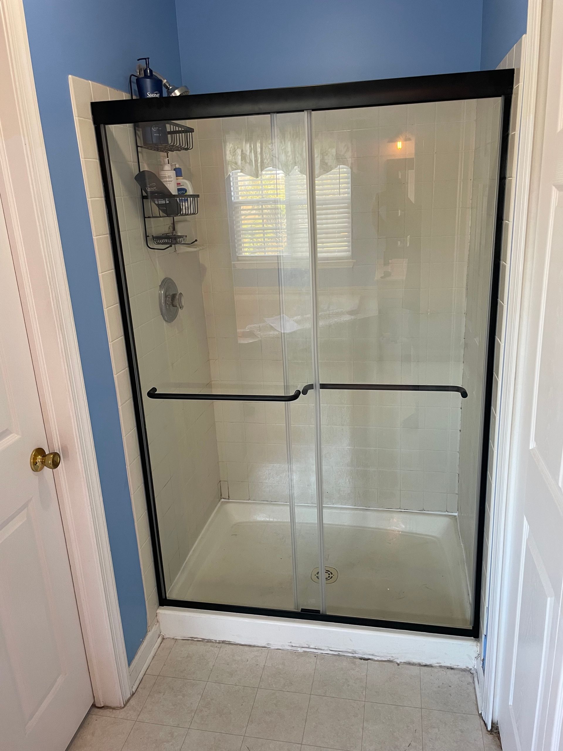 Shower stall with black framed glass doors, in a bathroom with blue walls.