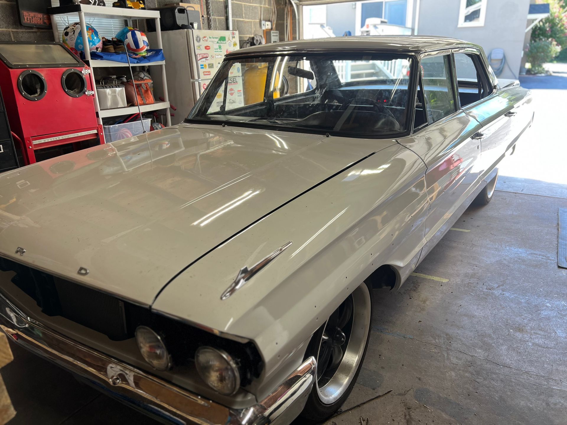 Light grey classic car parked in a garage with a black roof and black wheels.