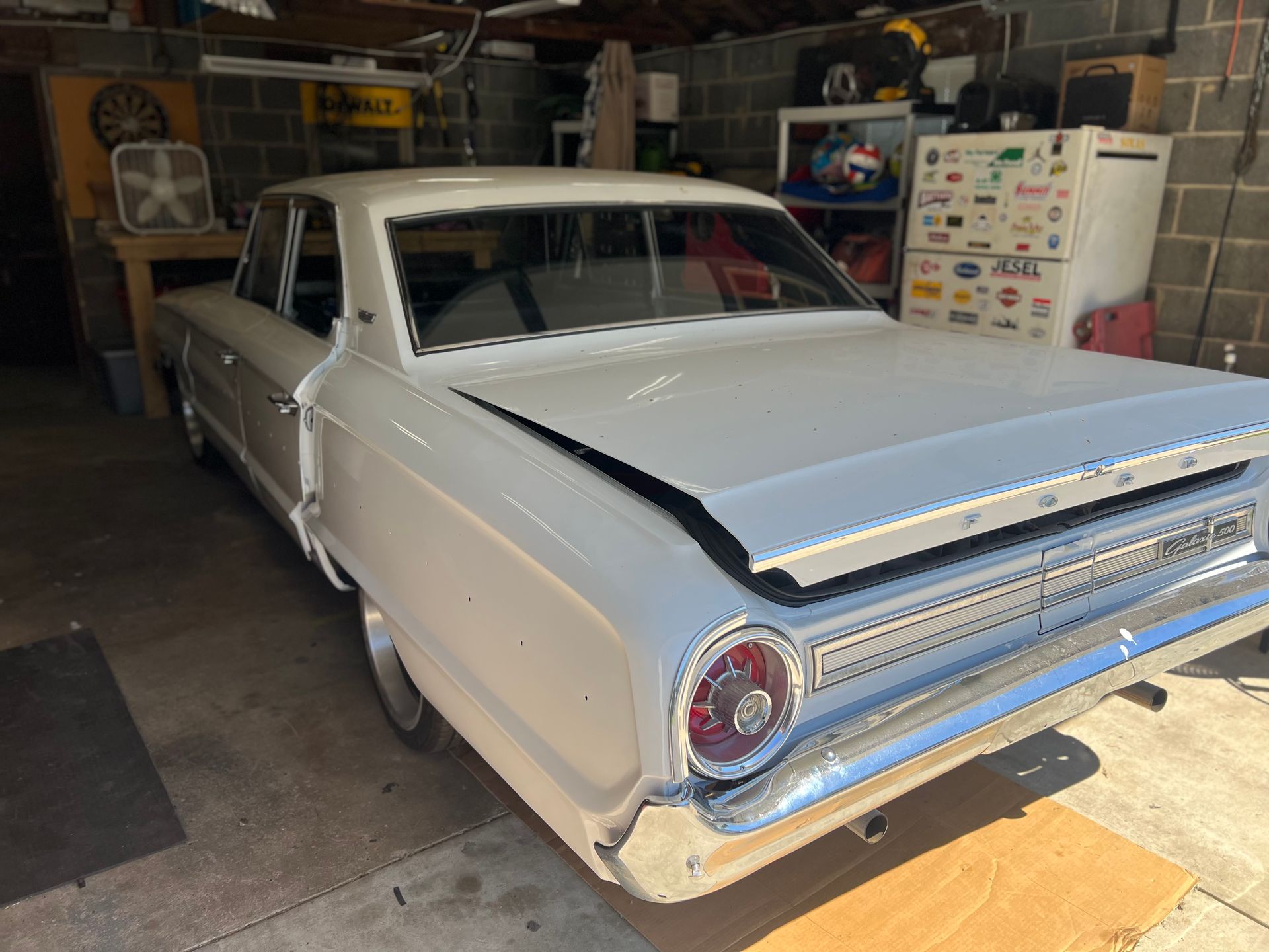 White classic car in a garage with hood open, chrome details.