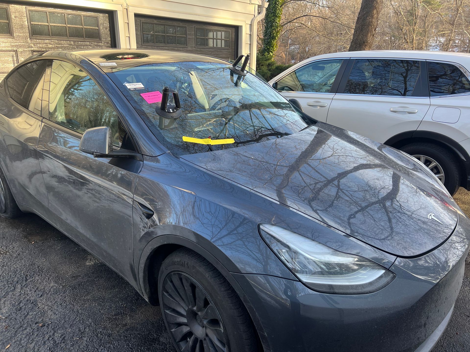 Gray Tesla Model Y car parked outside, with another white car next to it, garage in the background.