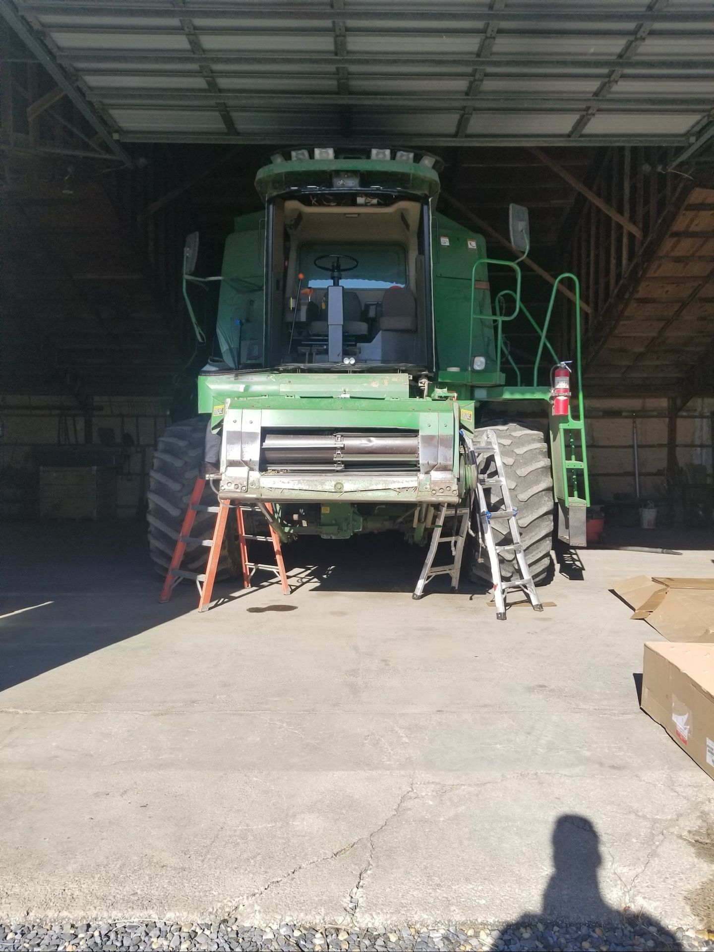 Green combine in a shed being worked on, supported by ladders.