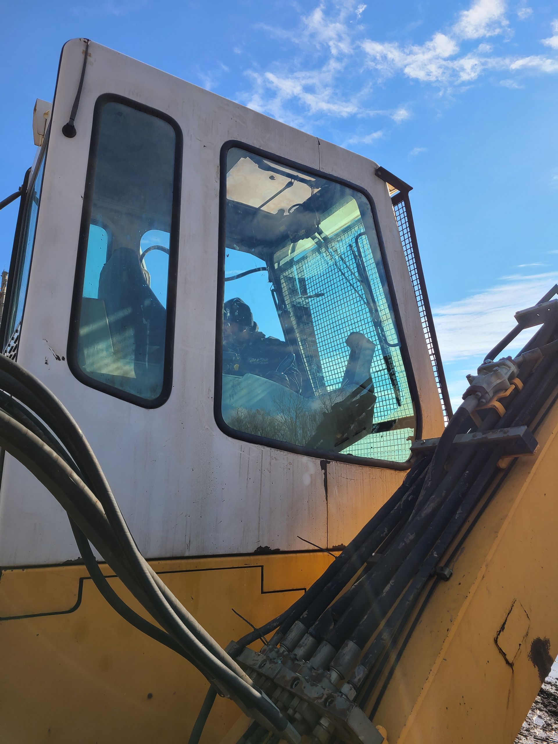 Yellow excavator cab with operator inside, blue-tinted windows, blue sky.
