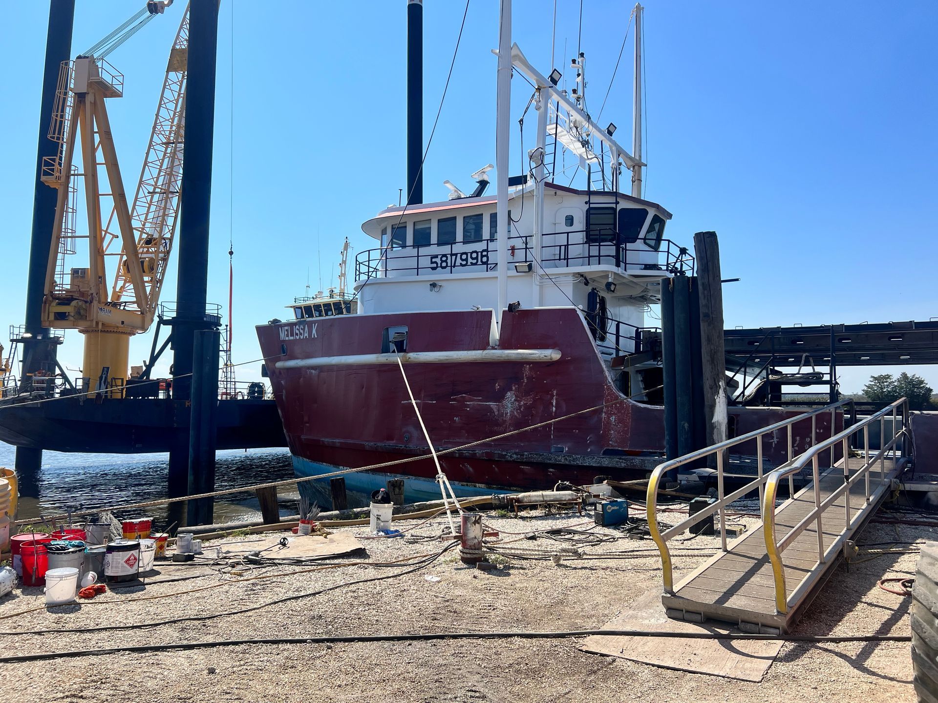A maroon and white fishing boat docked for repairs with a crane in the background.