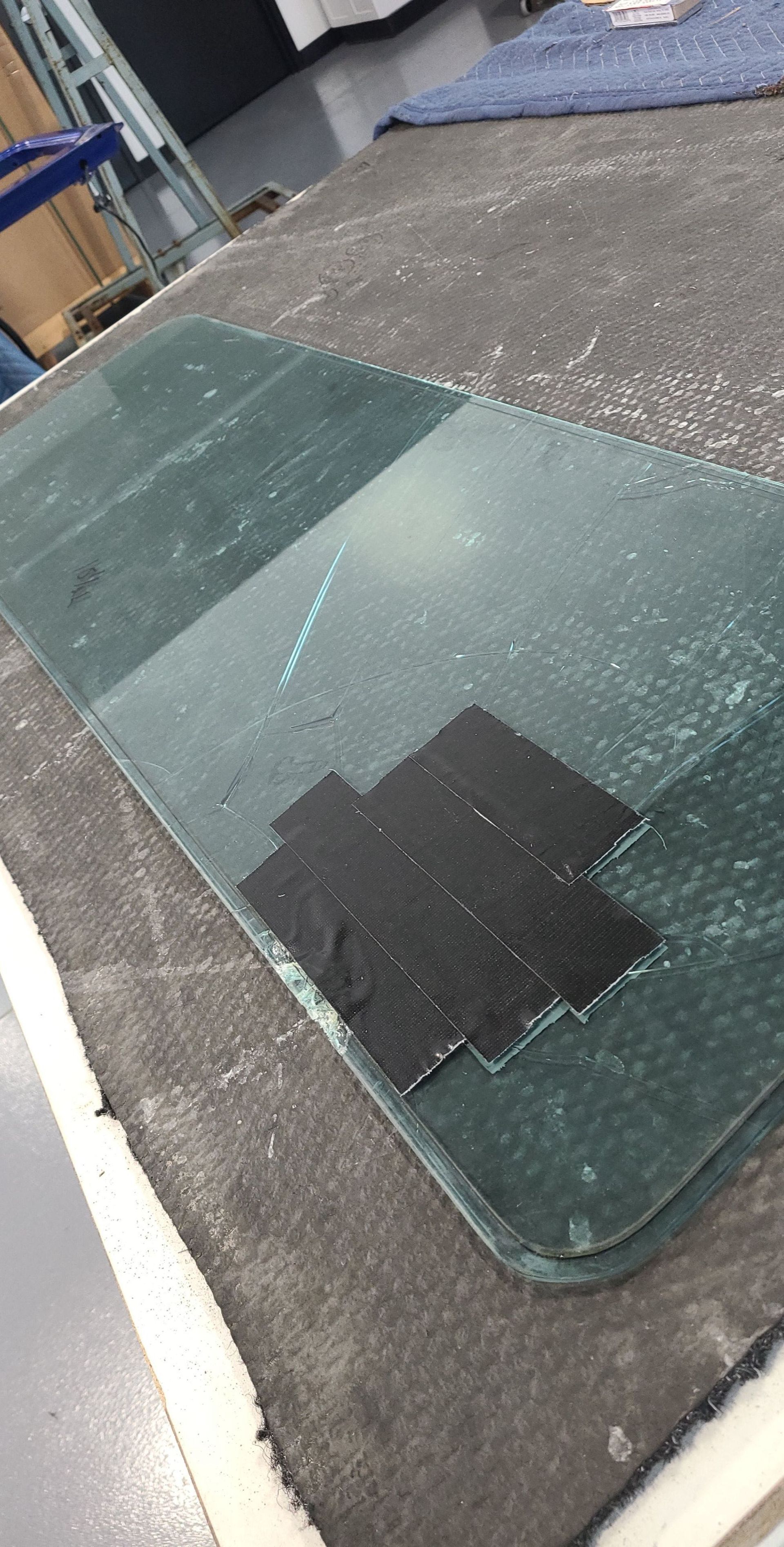 Cracked glass pane with black tape on a gray surface, possibly a work area.