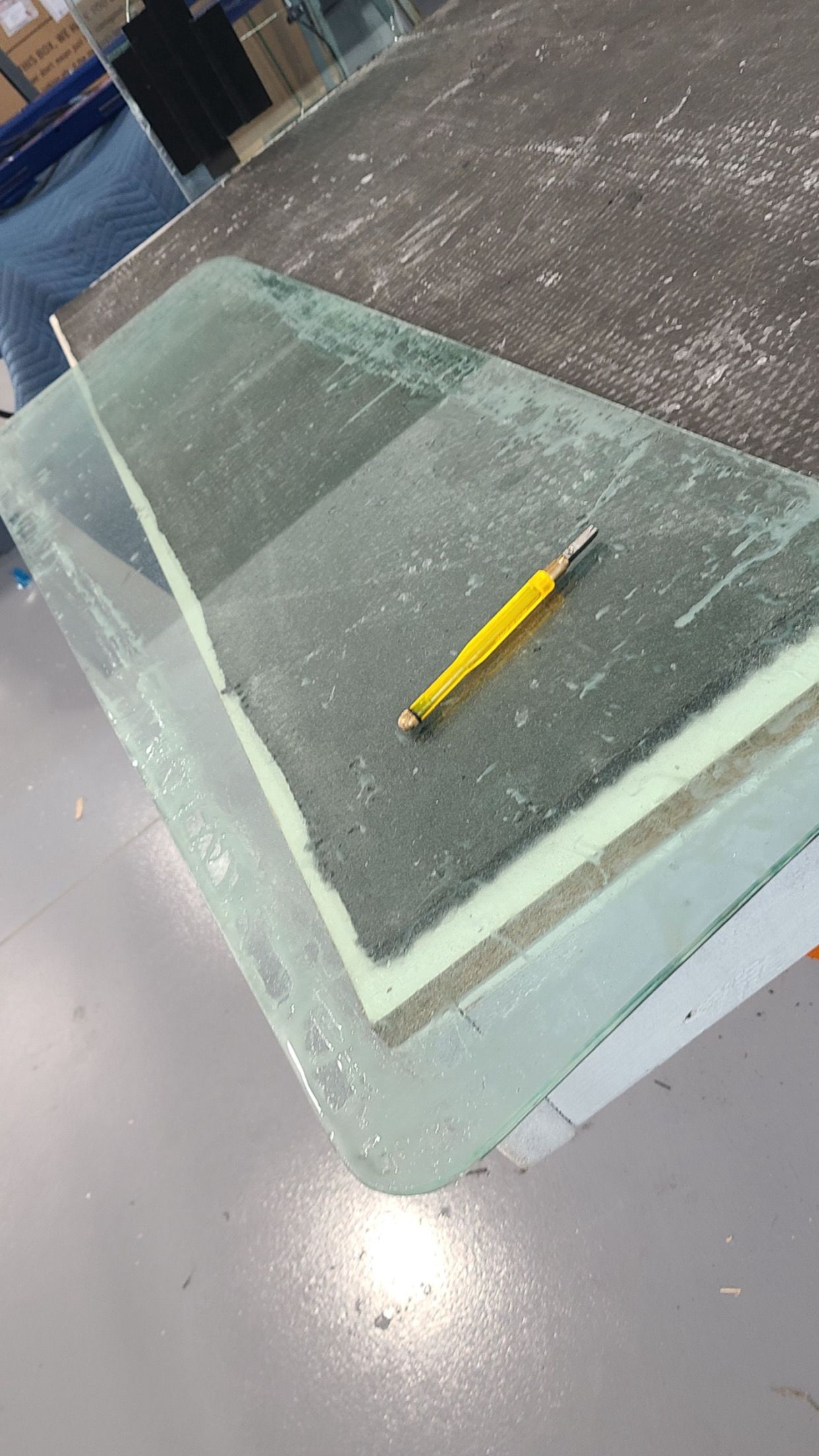 Glass panels stacked on a surface with a yellow utility knife on top.