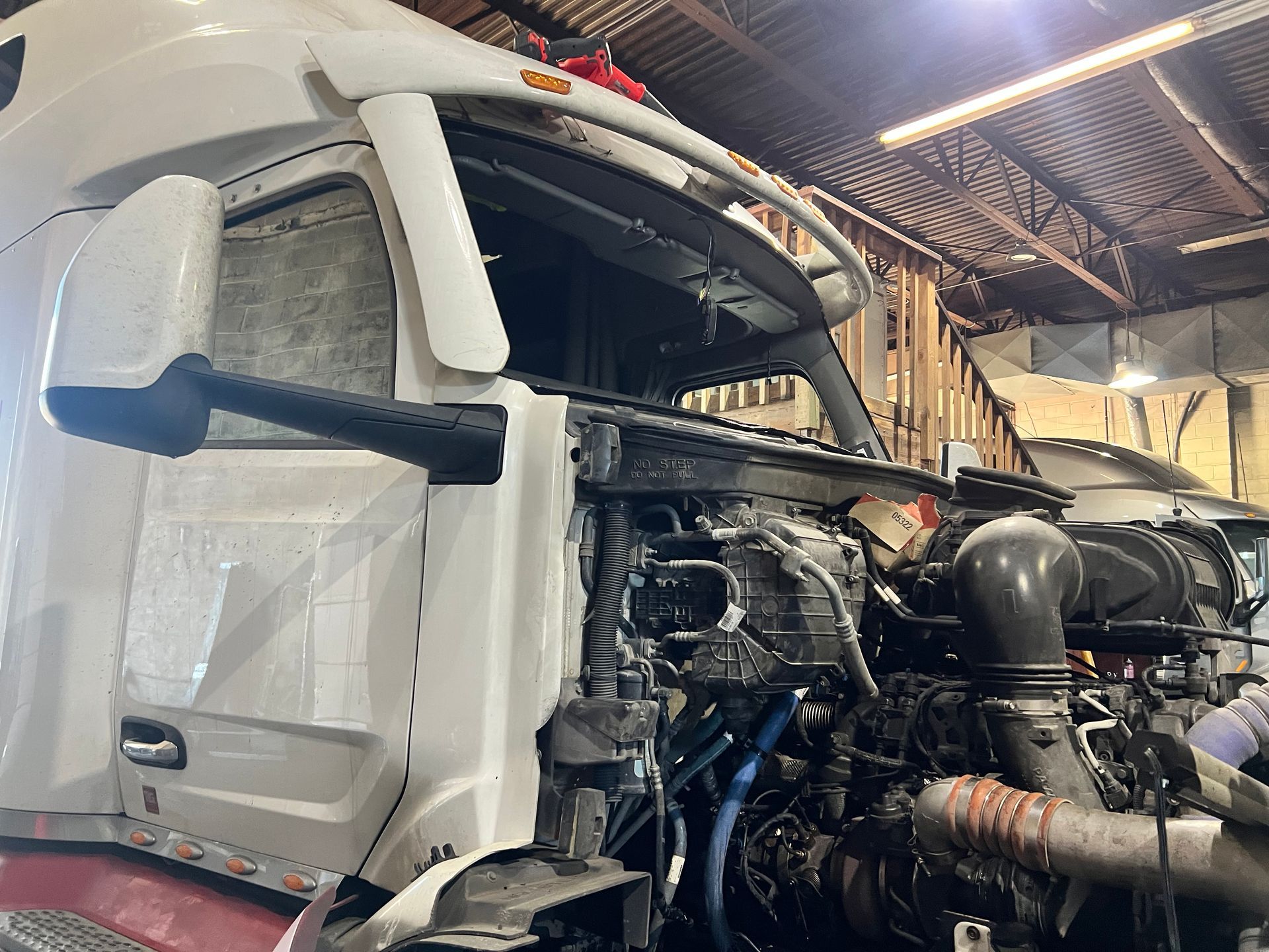 White semi-truck with open hood in a garage, revealing engine components.