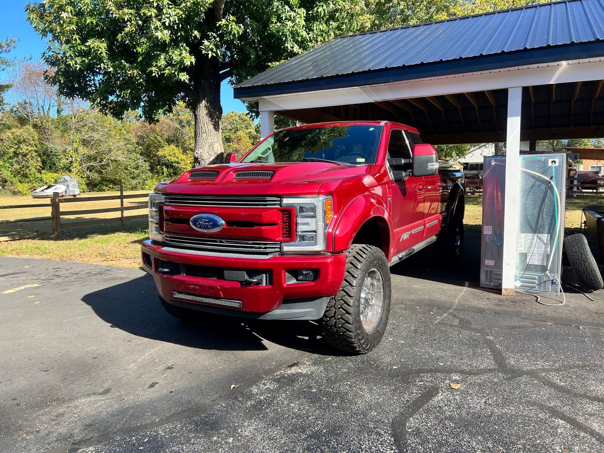 Red Ford truck parked under a carport on a sunny day.