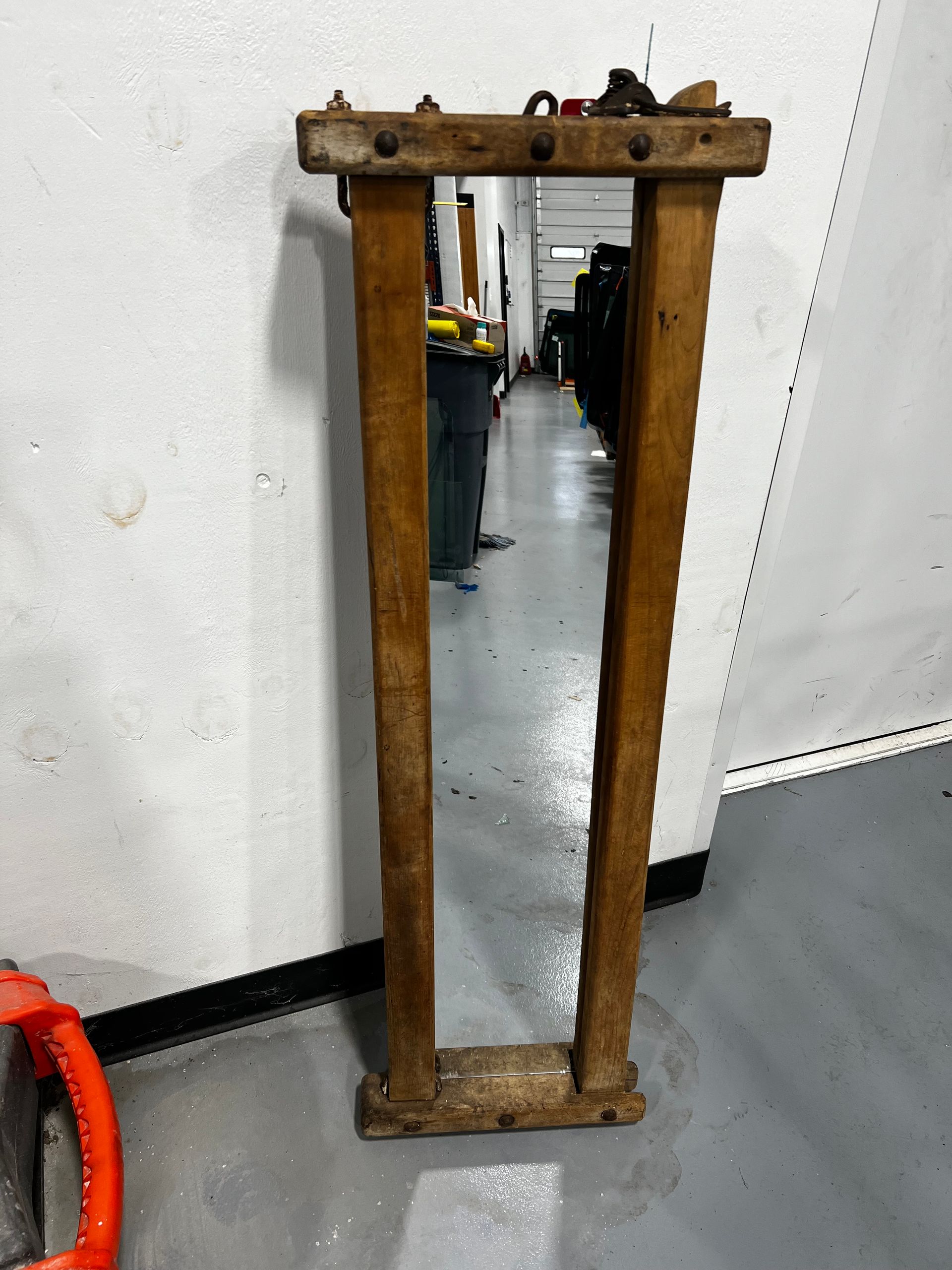 Tall rectangular wooden-framed mirror, weathered appearance, leaning against a white wall in a room.