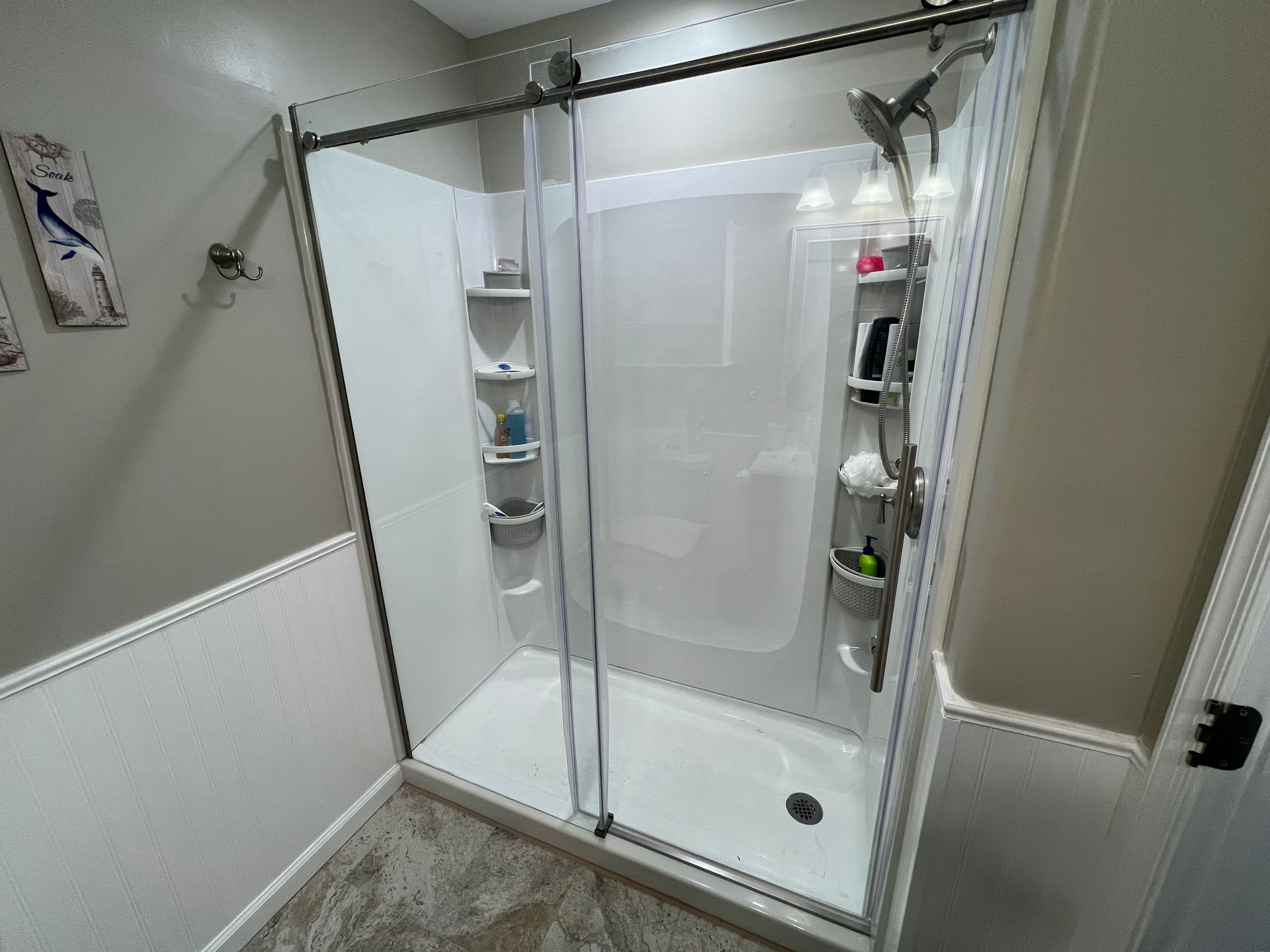 White-walled shower with glass sliding doors, shelving, and fixtures in a bathroom.