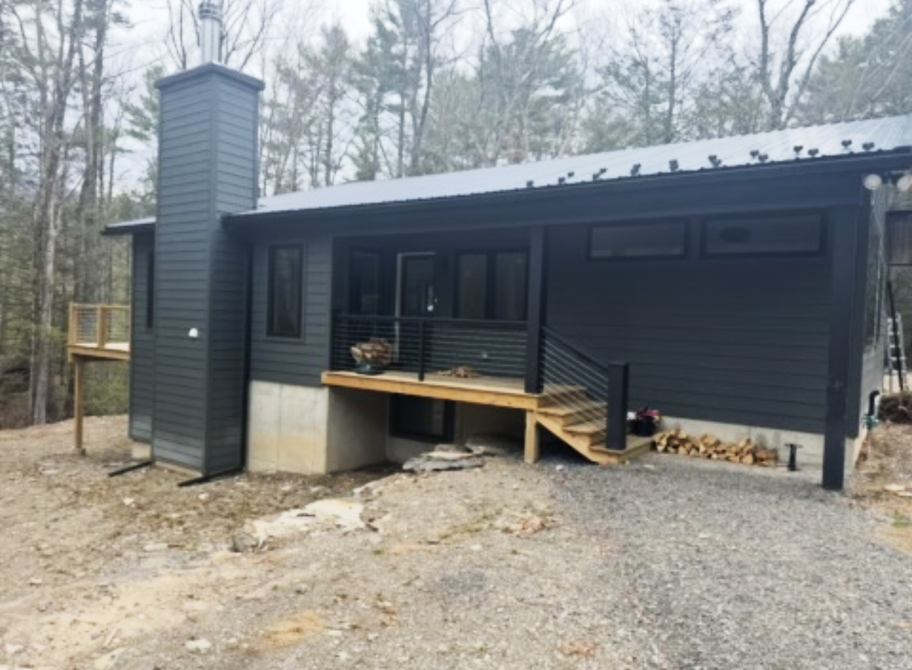 A small black house with a porch and stairs in the woods.
