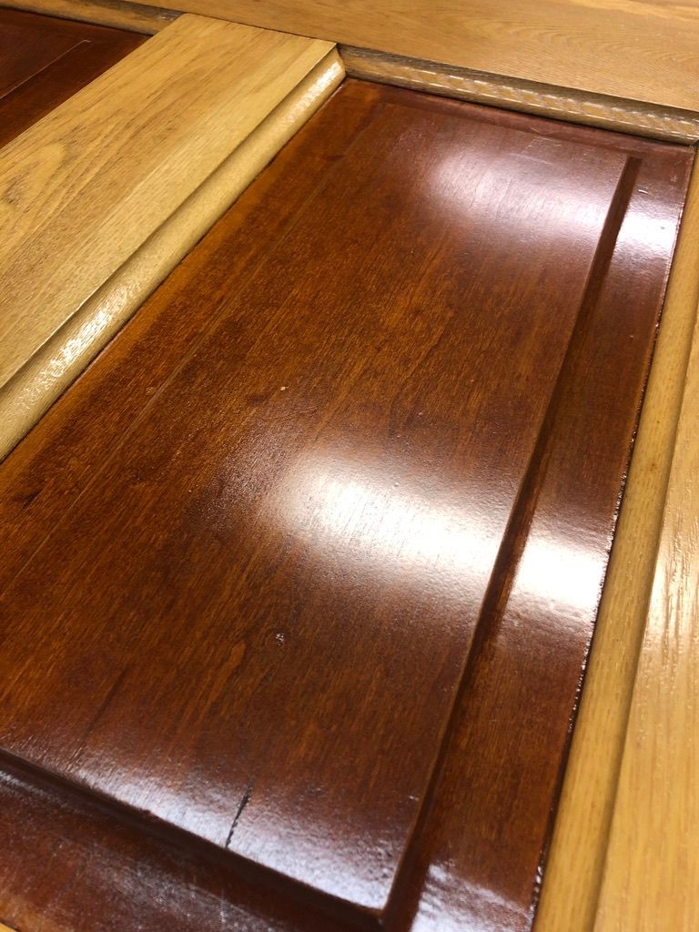 Close-up of a wooden cabinet door with a shiny, dark brown panel framed by lighter wood.