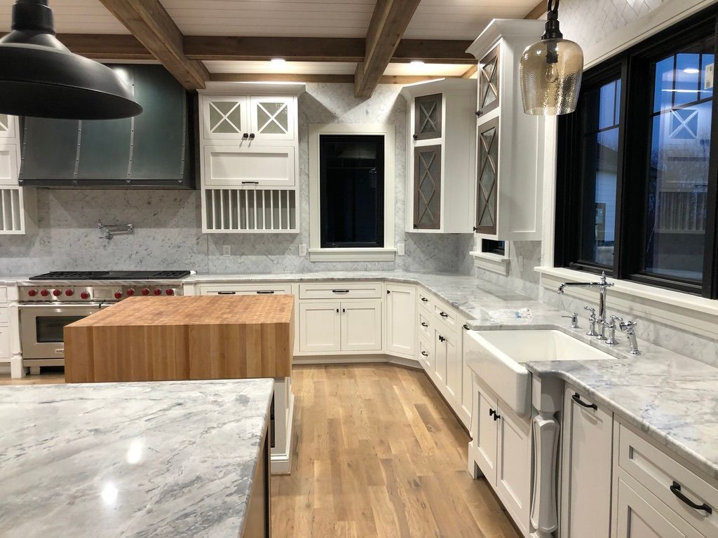 Stylish kitchen with white cabinets, marble countertops, wooden island, and exposed beams.