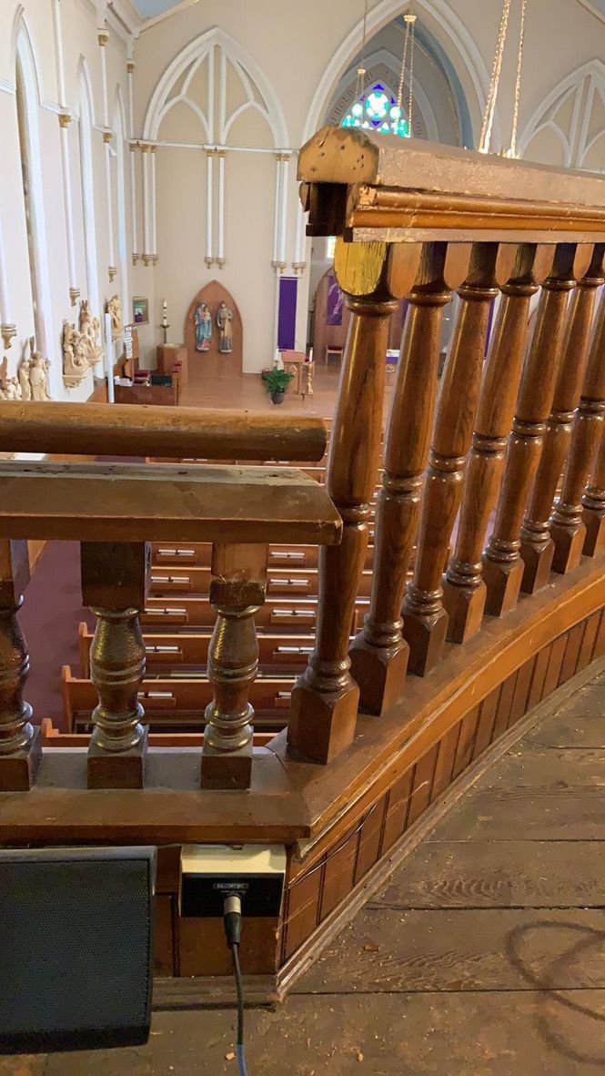 Wooden church railing with view of the interior: pews, altar, and stained glass windows.