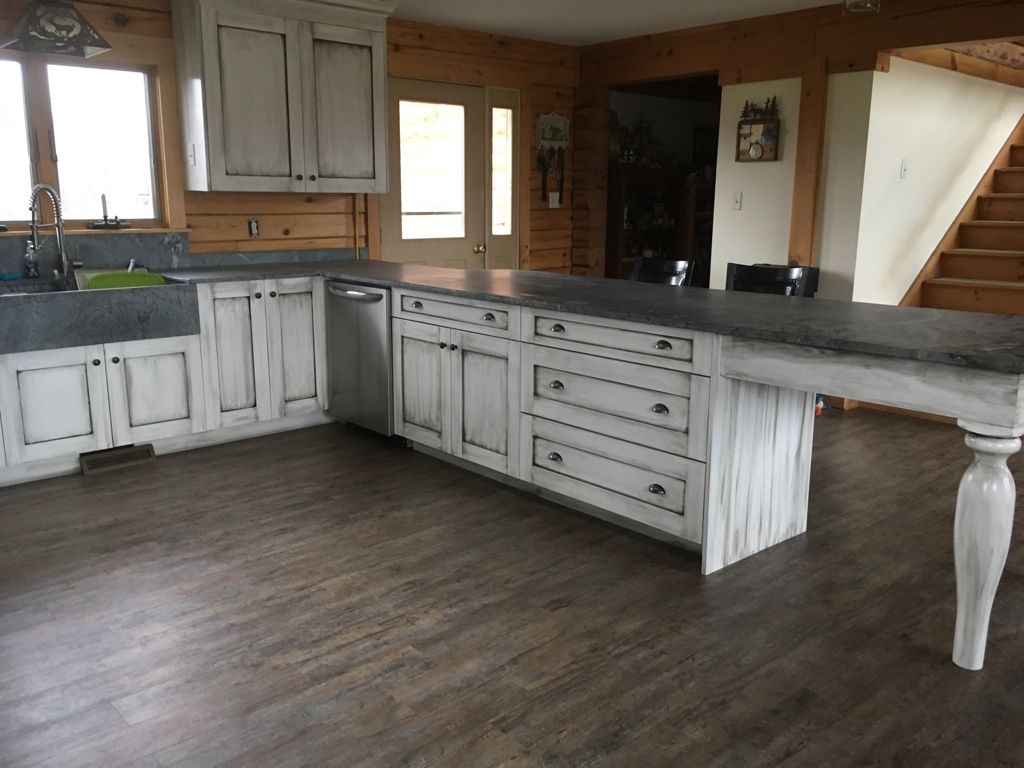 Rustic kitchen with white cabinets, gray countertop, and wooden floor.