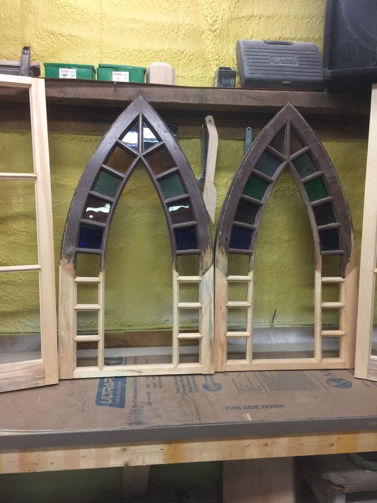 Two Gothic arched stained glass windows in wooden frames, on a workbench.