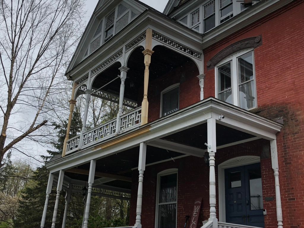 Two-story red brick house with white porch and decorative trim. Overcast sky.