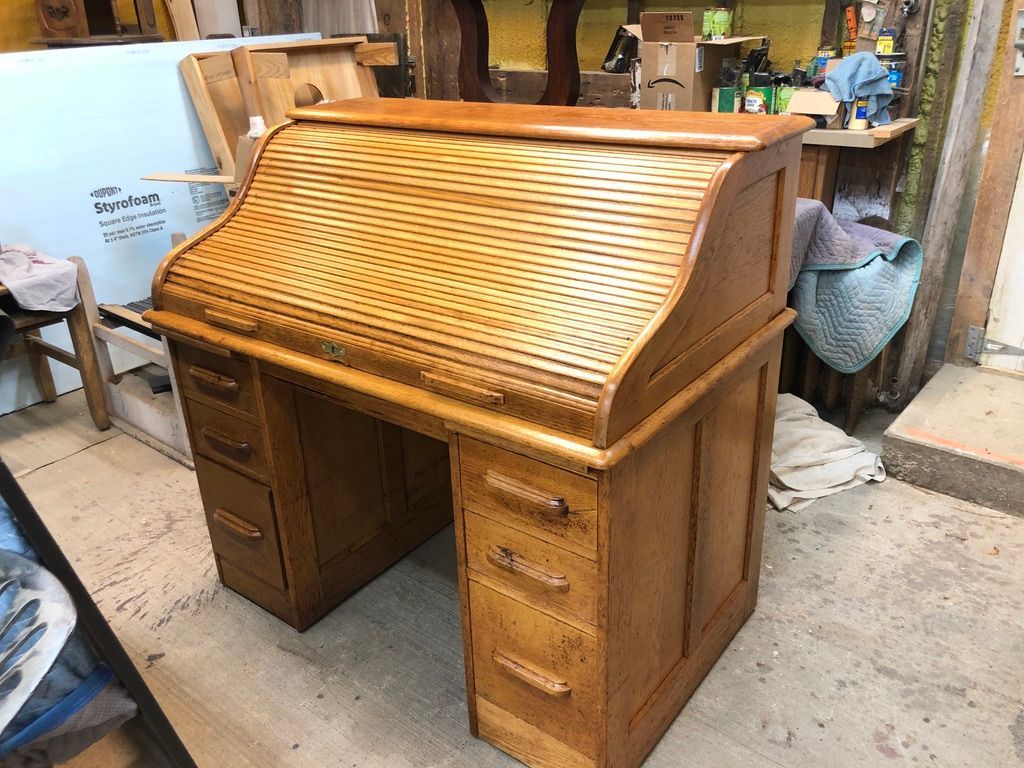 Wooden roll-top desk with multiple drawers in a workshop setting.