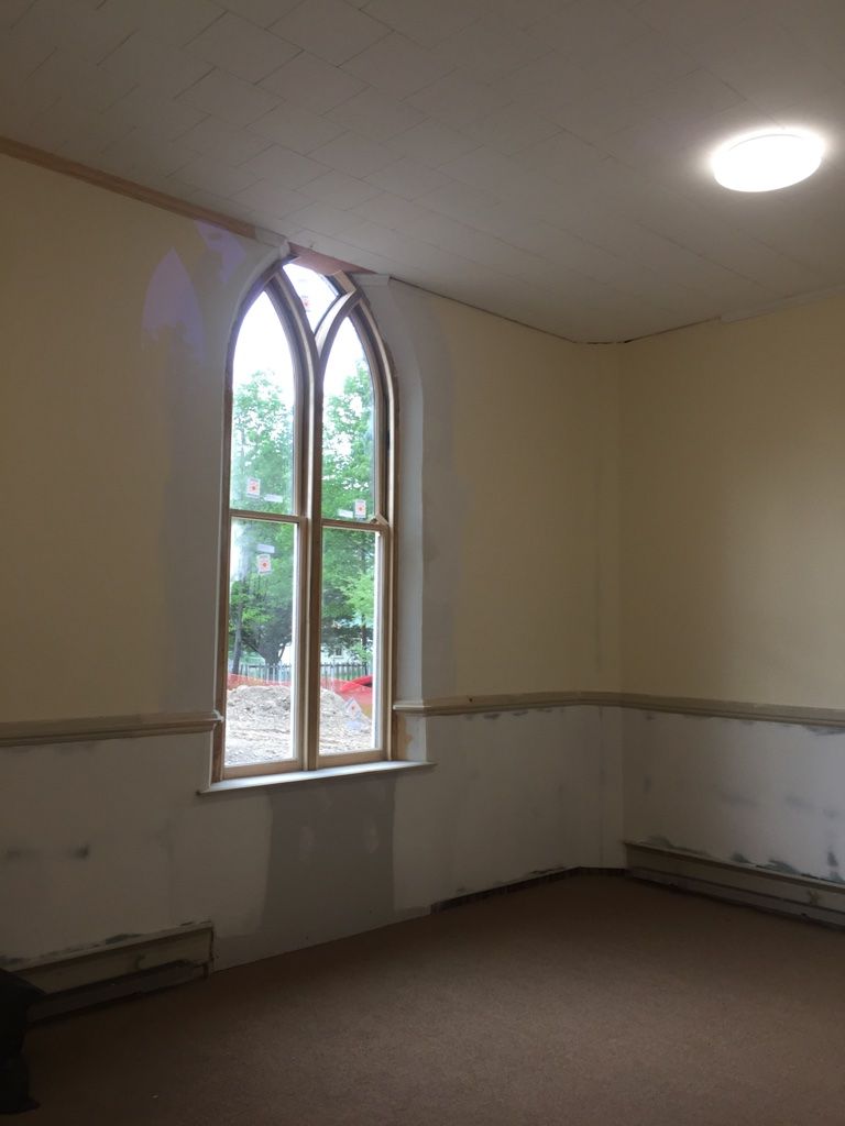 Interior of a room with a tall, arched window and a circular ceiling light. Cream walls, brown carpet.