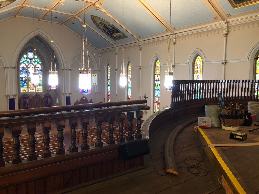 Interior church view with stained glass, ornate woodwork, and balcony.