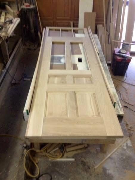Wooden door being assembled in a workshop, lying flat on a workbench, with glass panels and a door frame.