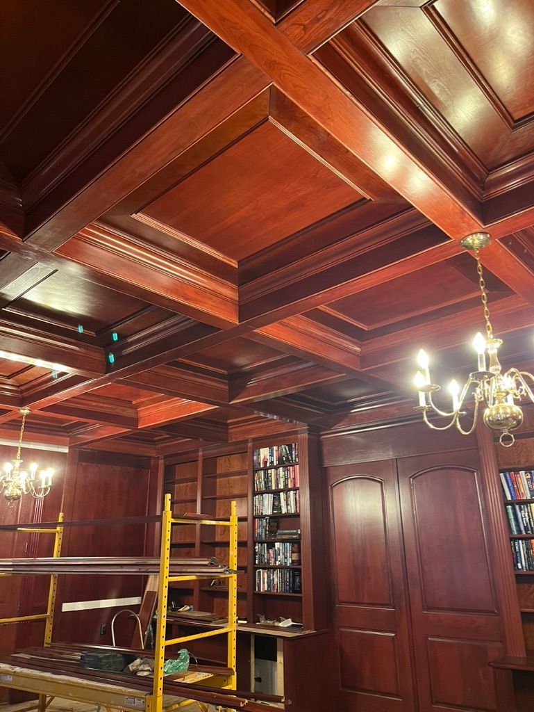 Dark wood paneled room with coffered ceiling. Scaffolding, two chandeliers, and a bookshelf visible.