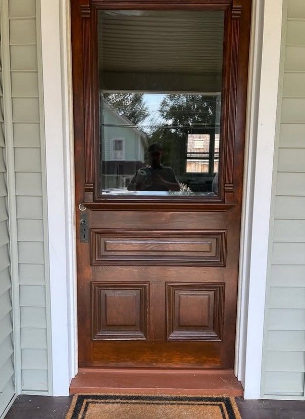 Wooden front door with glass panels and a brass handle, framed by light-colored siding.