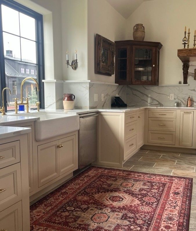 Bright kitchen corner with cream cabinets, large window, marble counters, and a red patterned rug