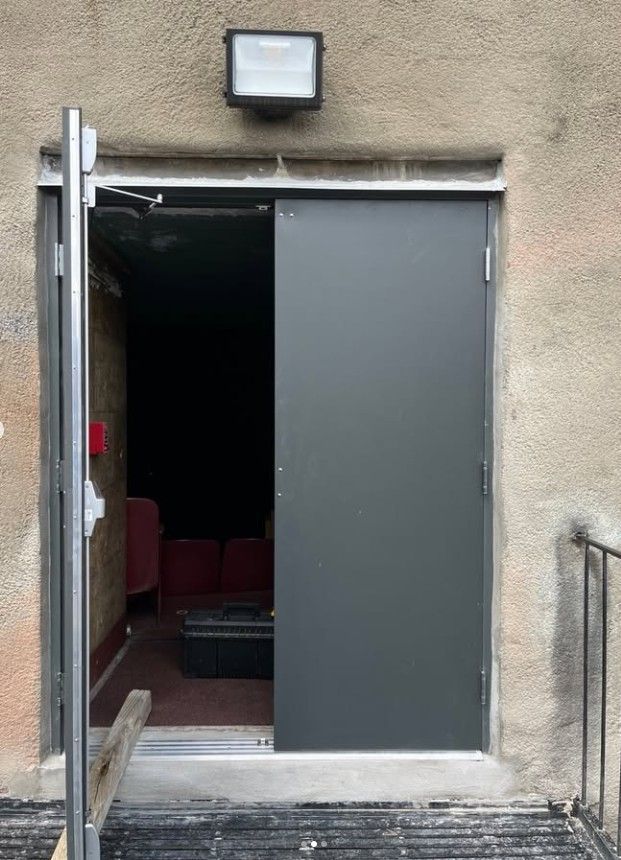 Open gray door to a dim interior, with an exterior wall light above and metal railing beside the steps.