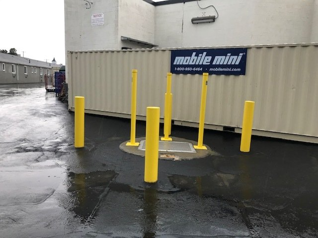 Yellow bollards outside a white mobile mini storage unit on a wet pavement