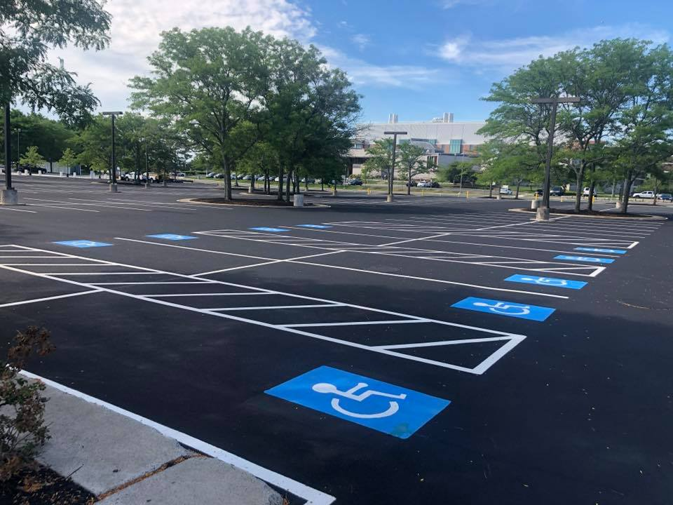 Empty parking lot with blue handicap parking spaces and trees under a partly cloudy sky