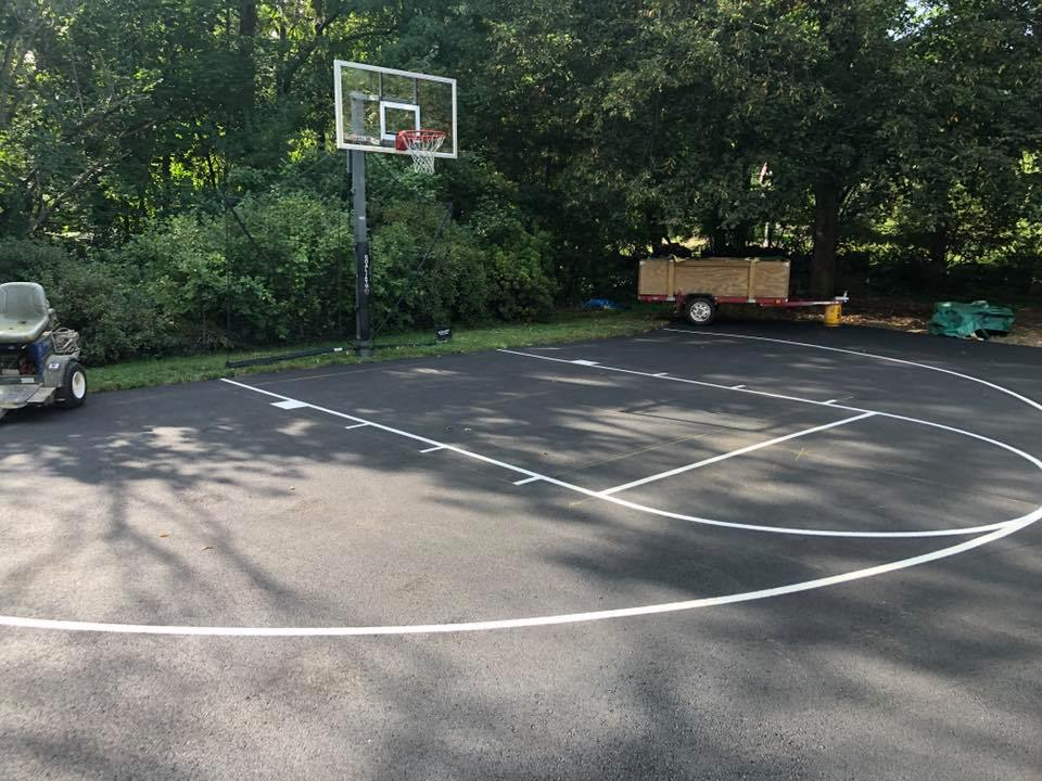 Empty outdoor basketball court with a hoop, white lines, and trees in the background