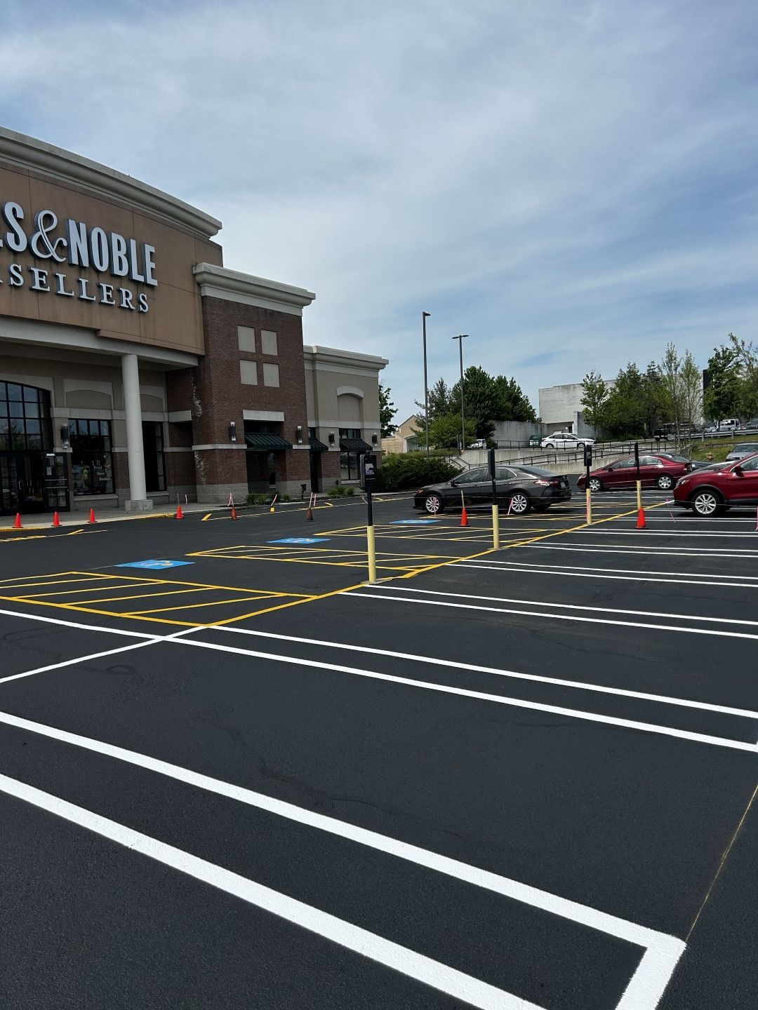 Parking lot outside a Barnes & Noble, with painted spaces, yellow bollards, and a red car nearby
