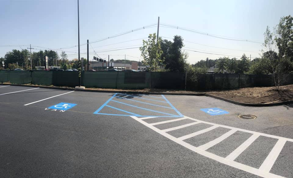 Empty accessible parking area with blue-striped markings and curb ramp beside a fenced lot